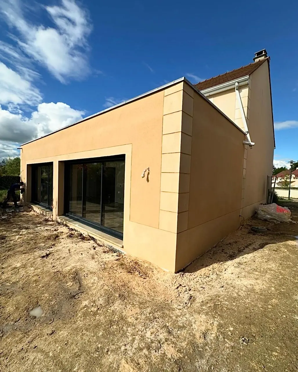 Extension maçonnée enduite avec grandes baies vitrées anthracite.