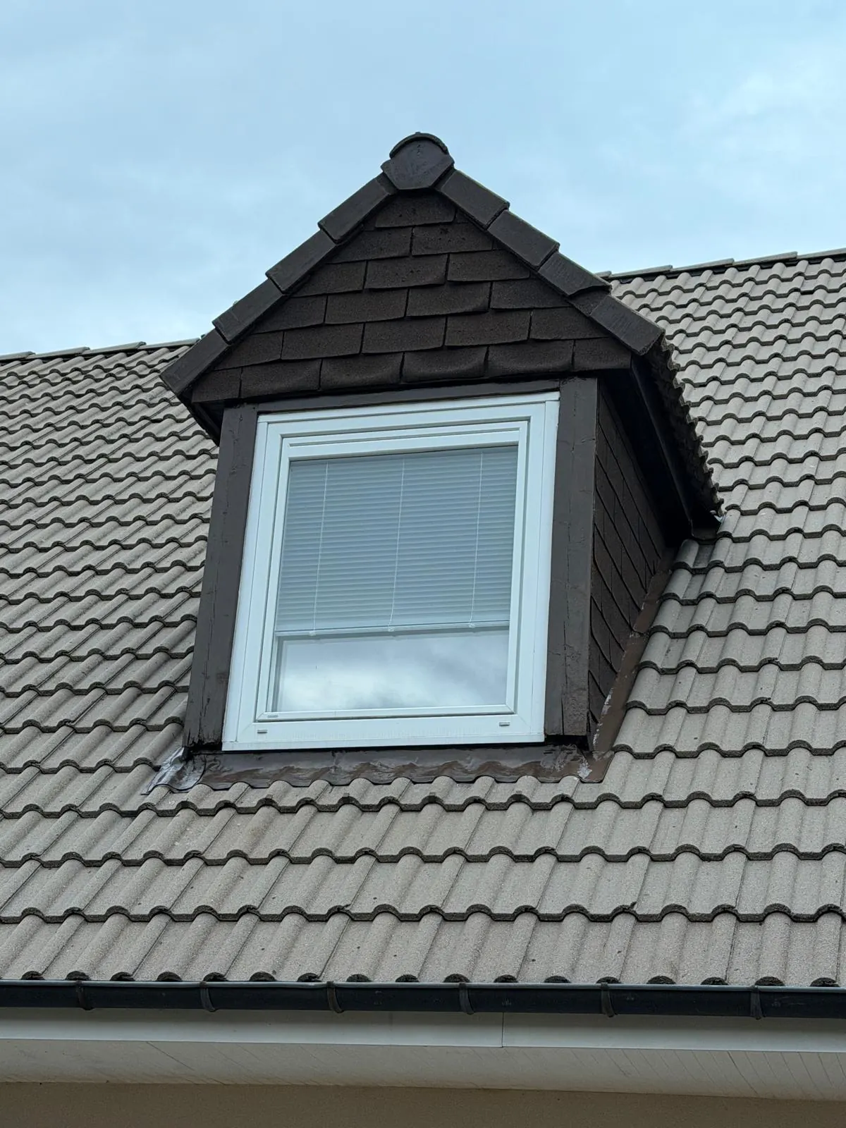 Lucarne intégrée à une couverture en tuiles sombres, avec ses raccords.